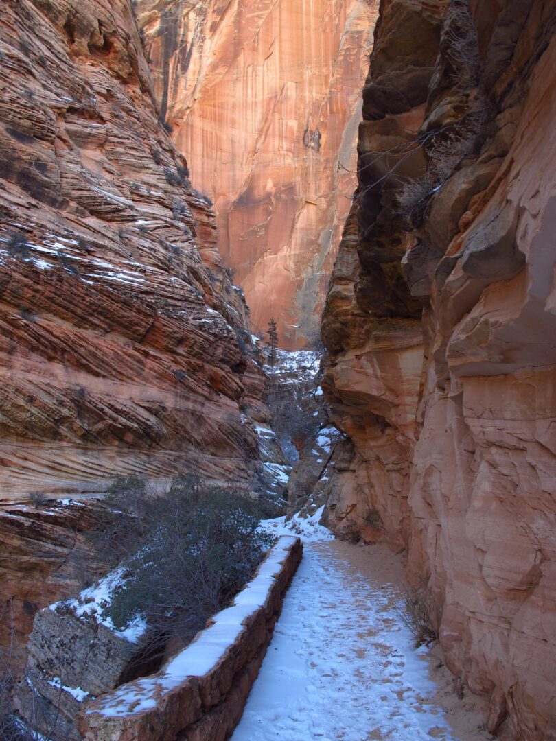 A narrow path through a canyon with snow on the ground.