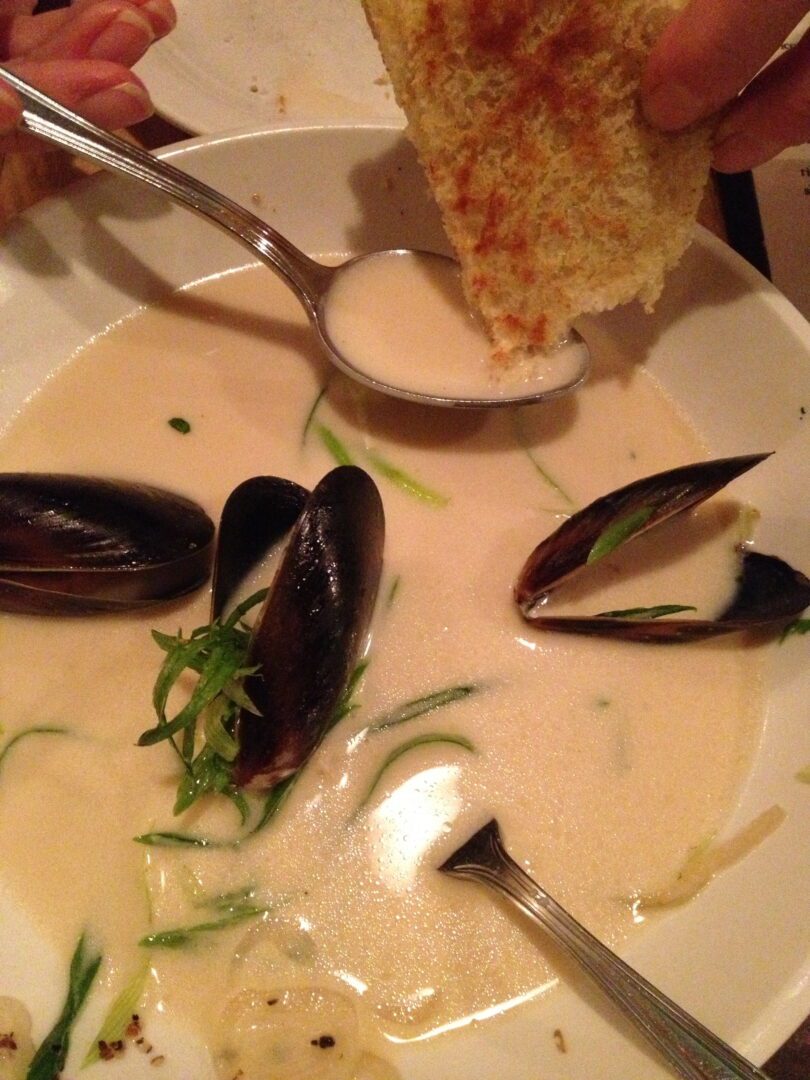 A bowl of soup with mussels in it.
