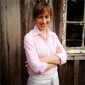 A woman in a pink shirt standing in front of a wooden building.