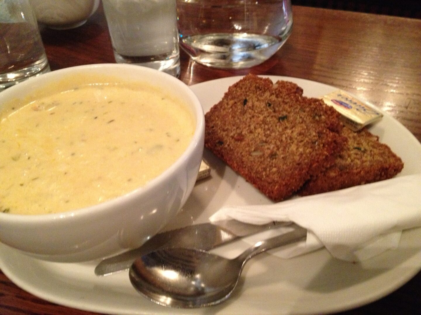 A white plate with a bowl of soup and bread.