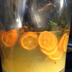 A glass pitcher filled with orange slices and rosemary.