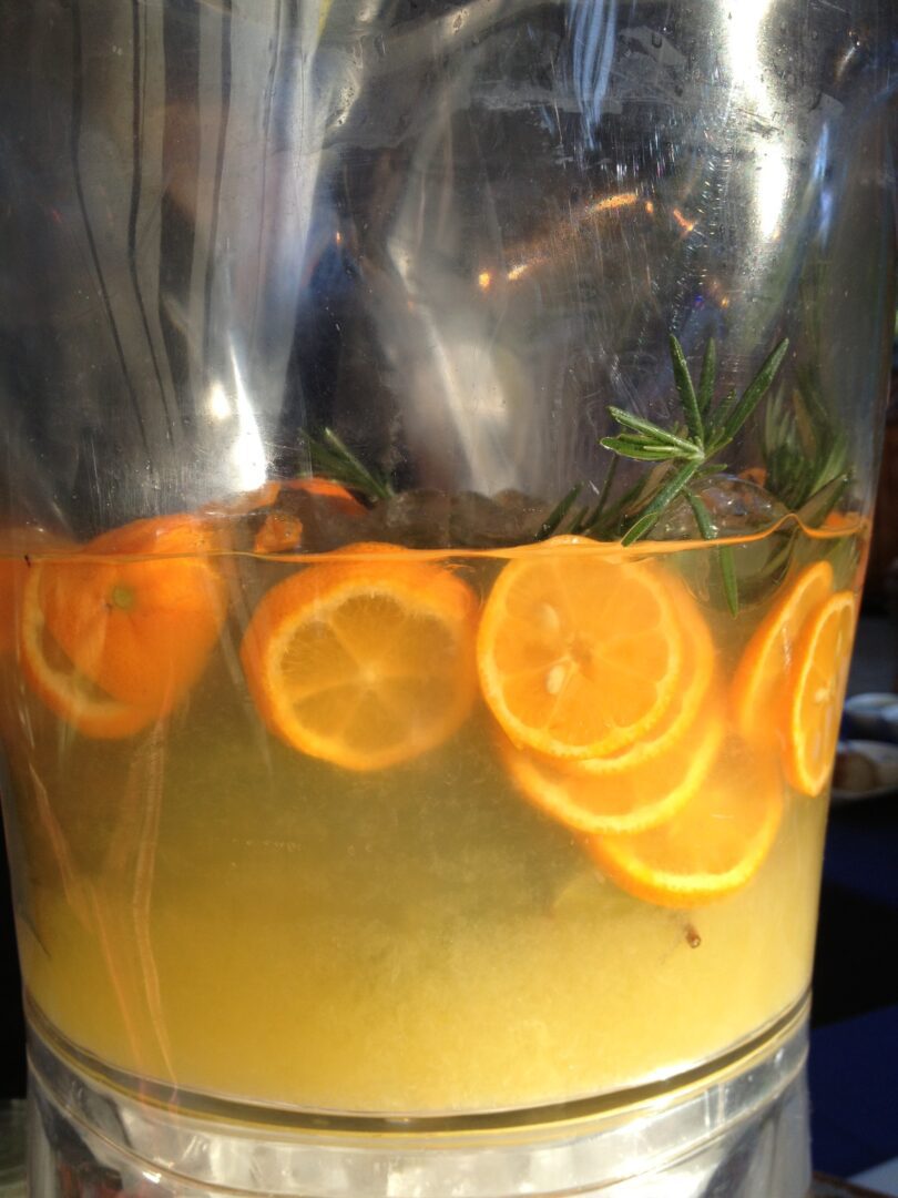A glass pitcher filled with orange slices and rosemary.