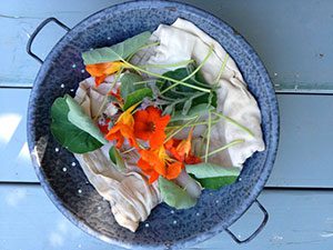 A bowl filled with flowers and leaves on a wooden table.