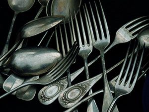 A pile of silver spoons and forks on a black surface.