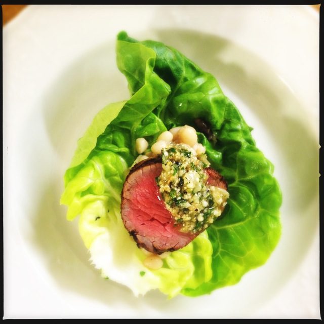 A white plate with a steak and lettuce on it.