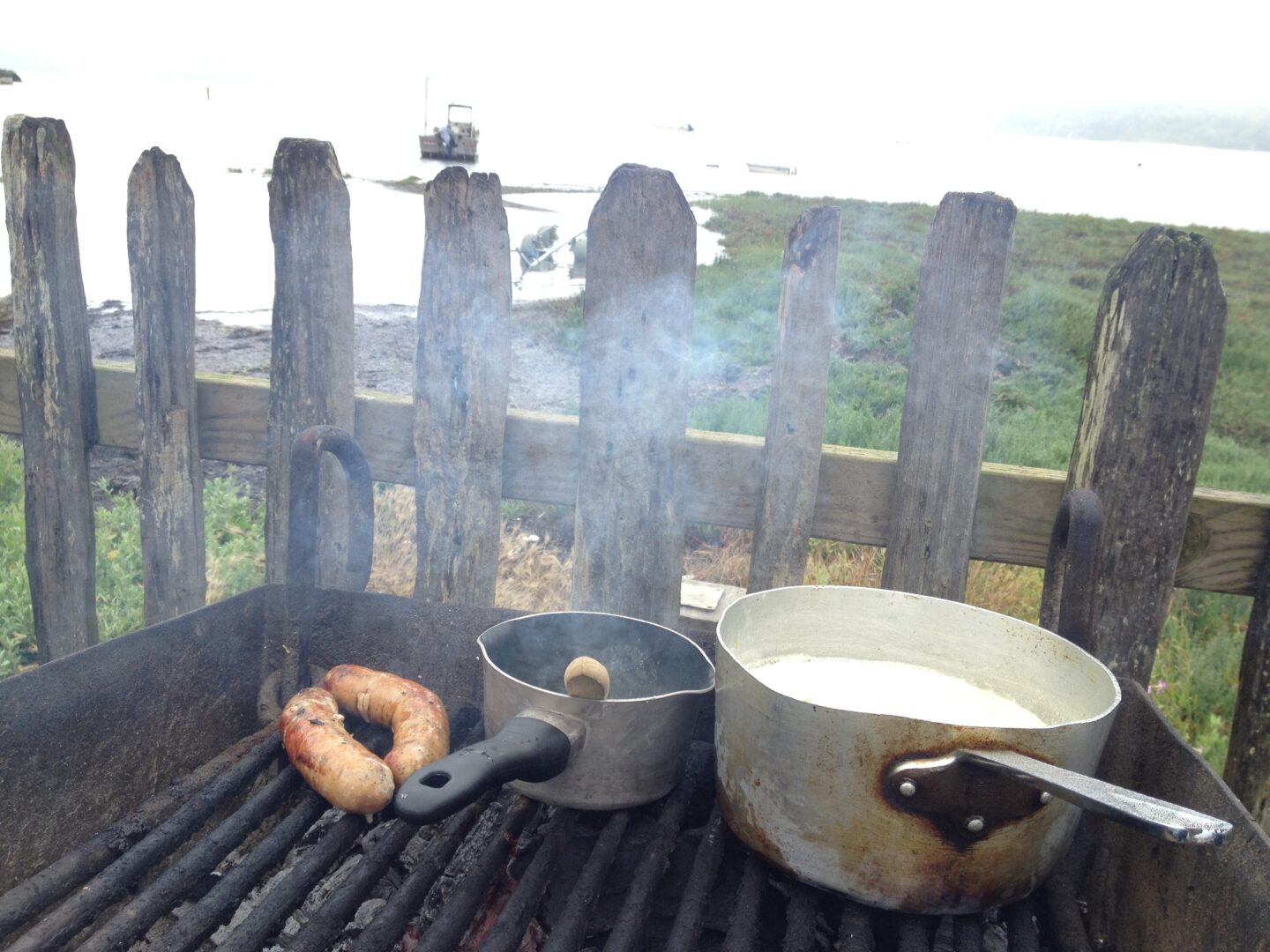 A grill with sausages and a pot of milk.