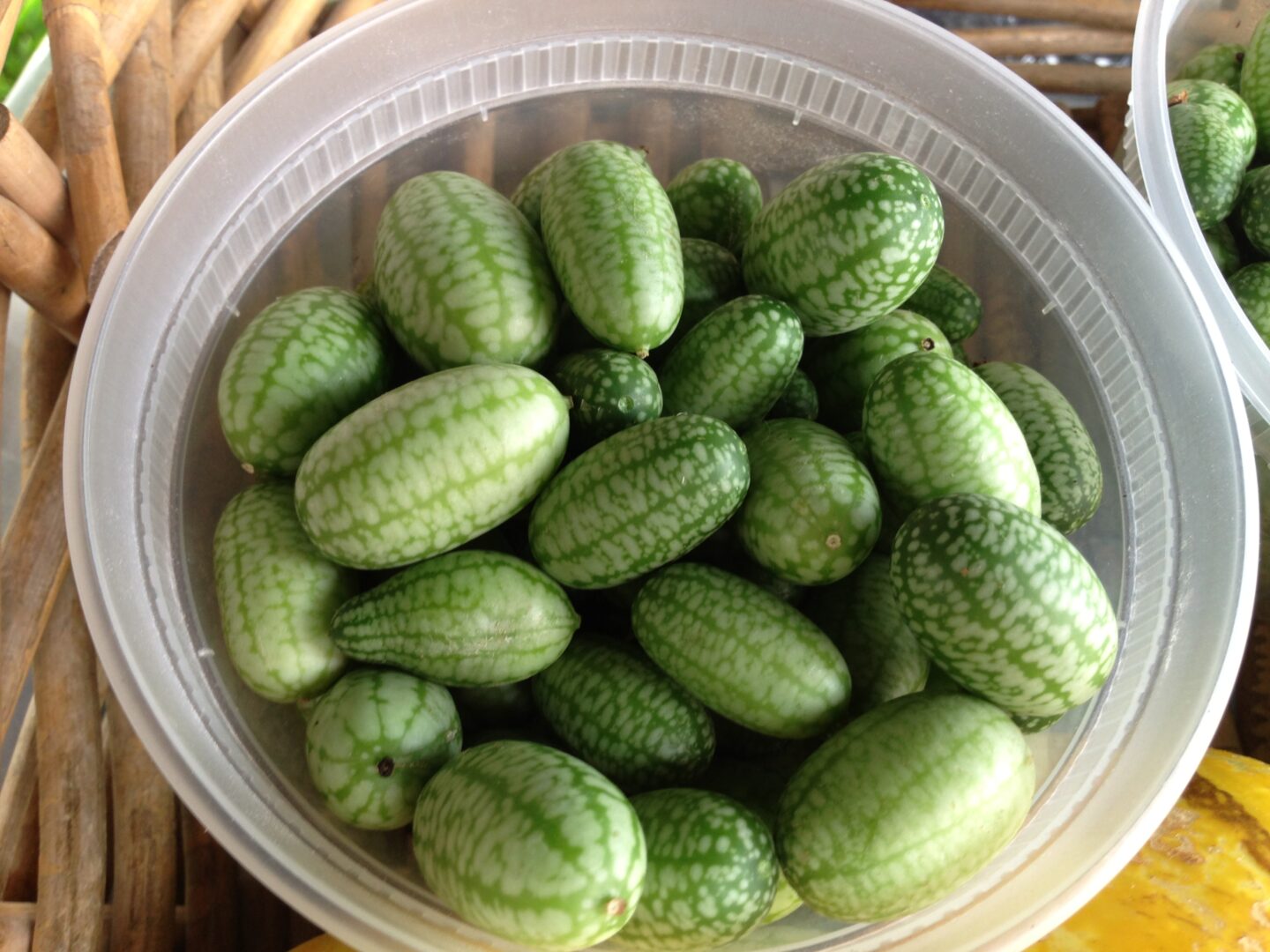 A bunch of green fruits in plastic bowls on a wicker basket.