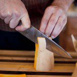 A man cutting a piece of cheese on a cutting board.