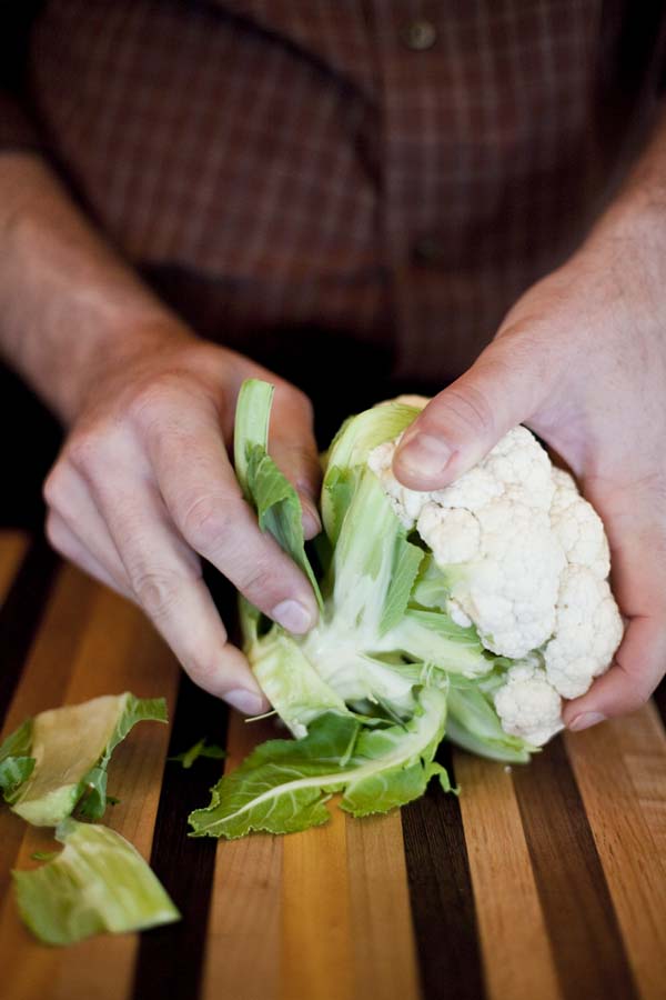 A man slicing a head of cauliflower on a cutting board.
