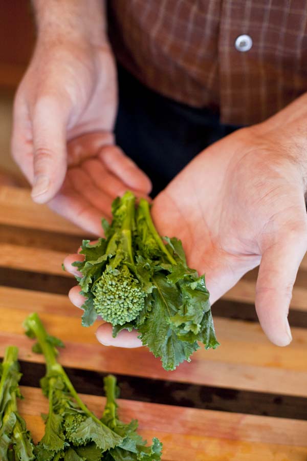 A man is holding a bunch of broccoli on a cutting board.