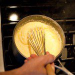 A person is whisking something in a pan on a stove.