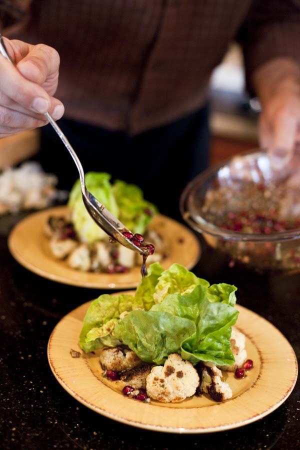 A man is pouring pomegranate dressing onto a plate of lettuce.
