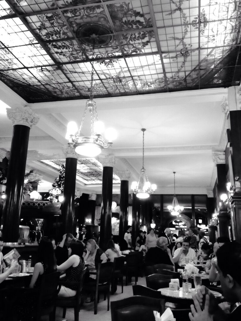 A black and white photo of a restaurant with people sitting at tables.