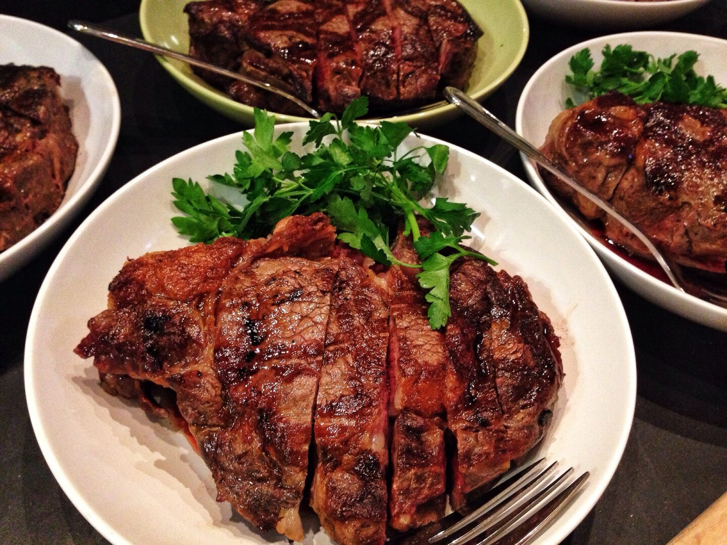 Four bowls of grilled steak with parsley on a table.