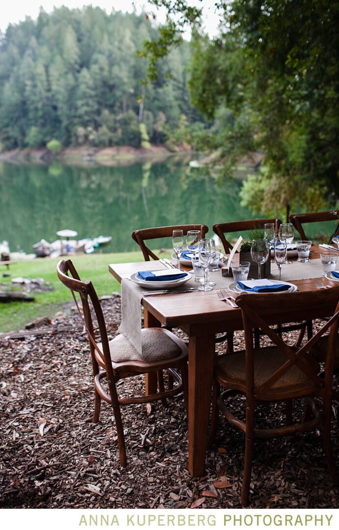 A wooden table set in a wooded area near a lake.