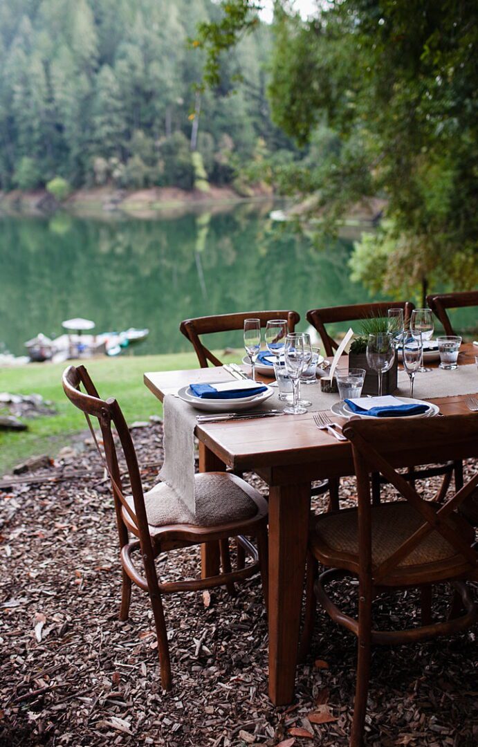 A wooden table set in a wooded area with a view of a lake.