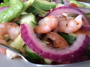 A plate of shrimp salad with tomatoes, cucumbers and onions.