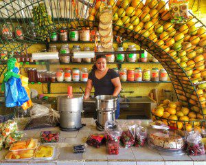 A woman standing behind a counter full of fruit.