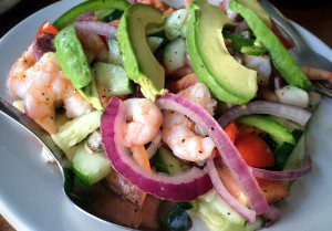 A plate of shrimp salad with tomatoes, onions and avocado.