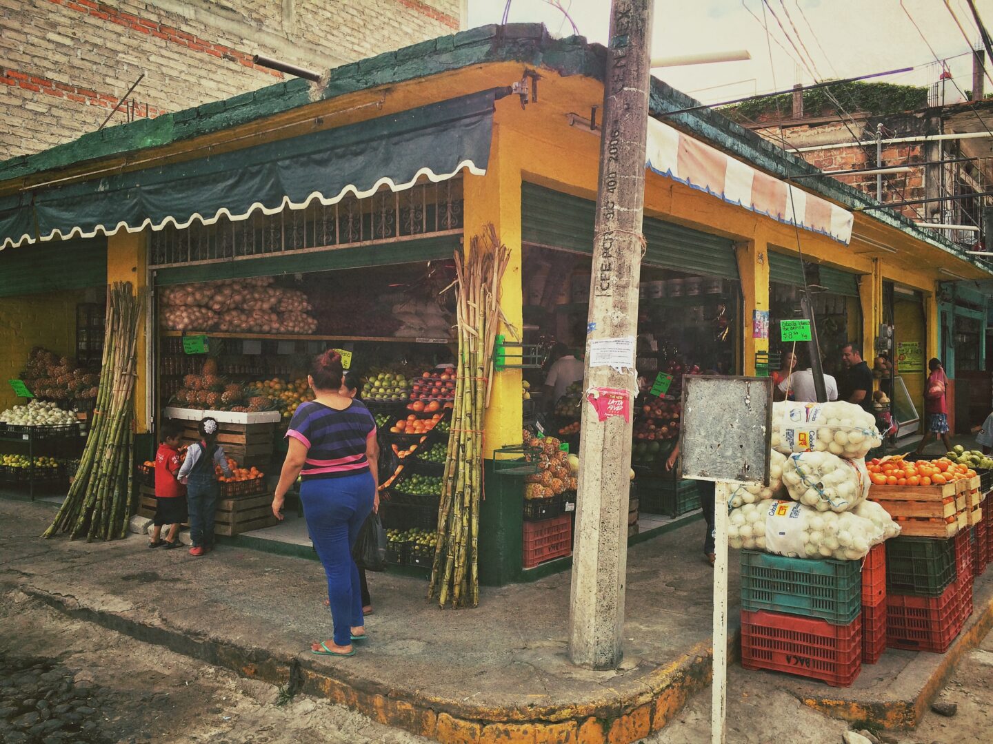 A woman walking past a fruit and vegetable stand.
