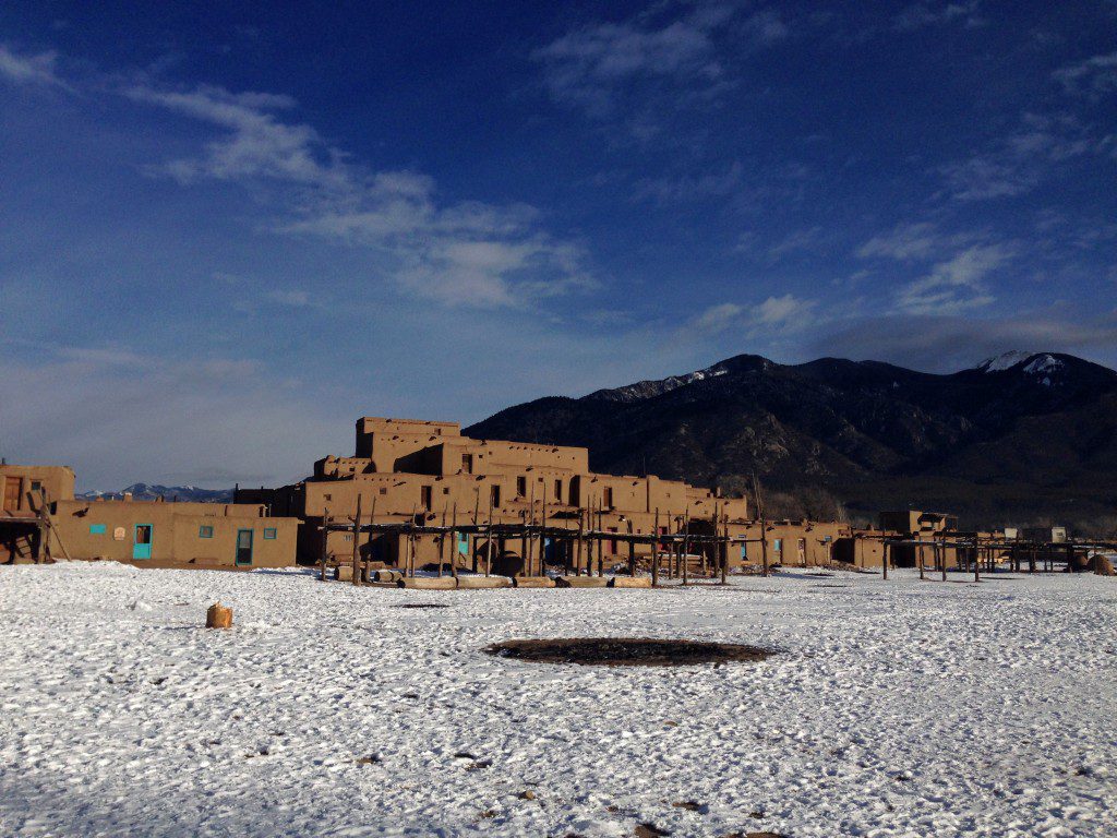 An adobe building in the snow with mountains in the background.