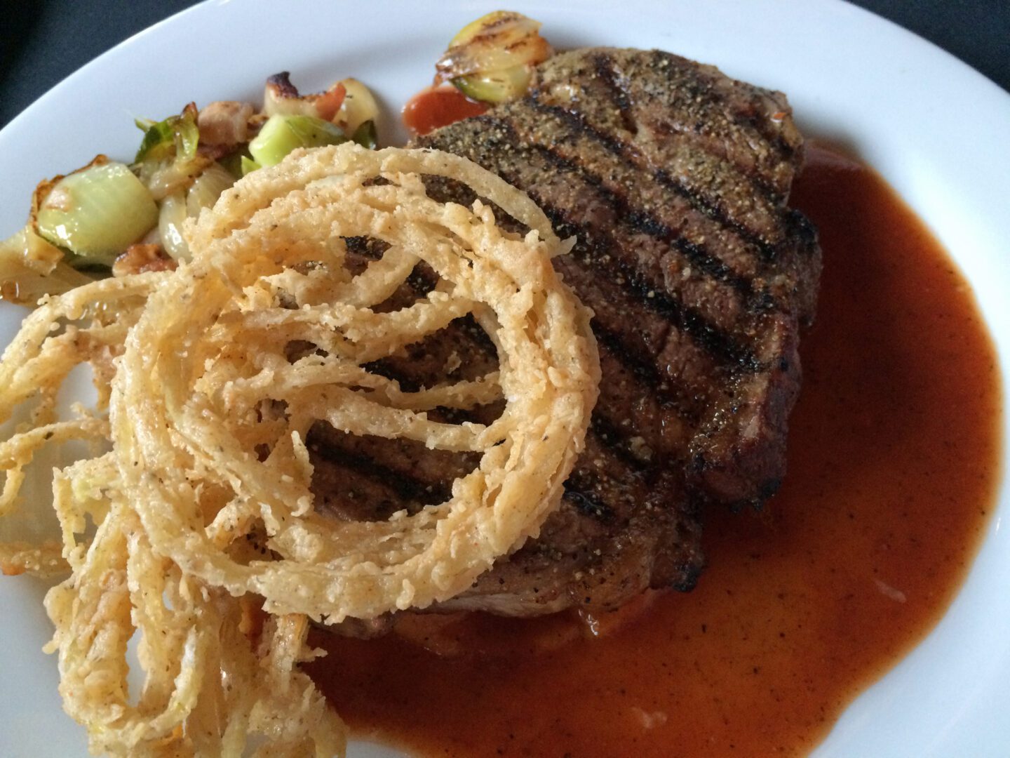 A steak with onion rings and sauce on a plate.