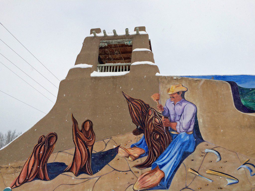 An adobe building with a mural of a man riding a horse.