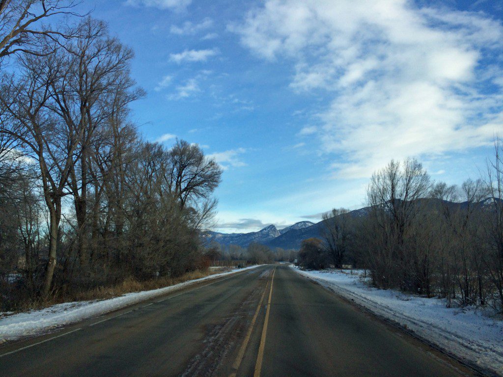 A snowy road with trees and mountains in the background.