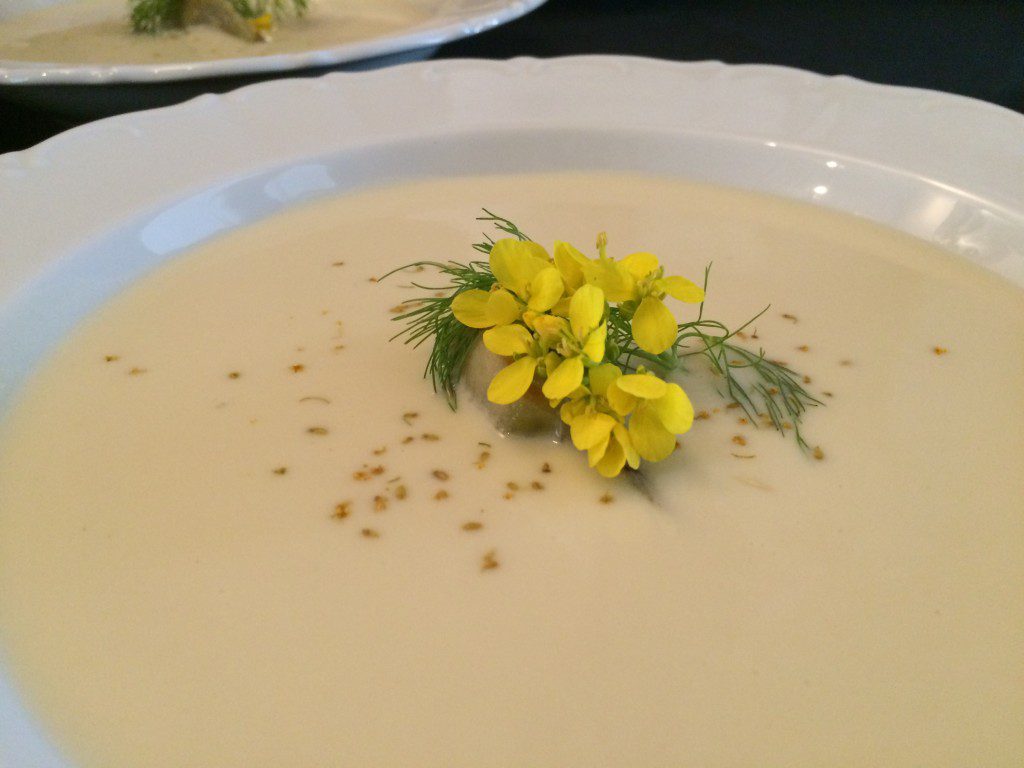 A white bowl of soup with yellow flowers on it.