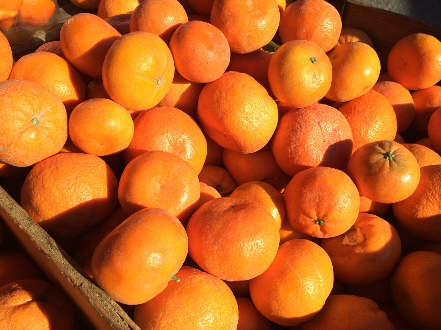 A pile of oranges in a wooden crate.