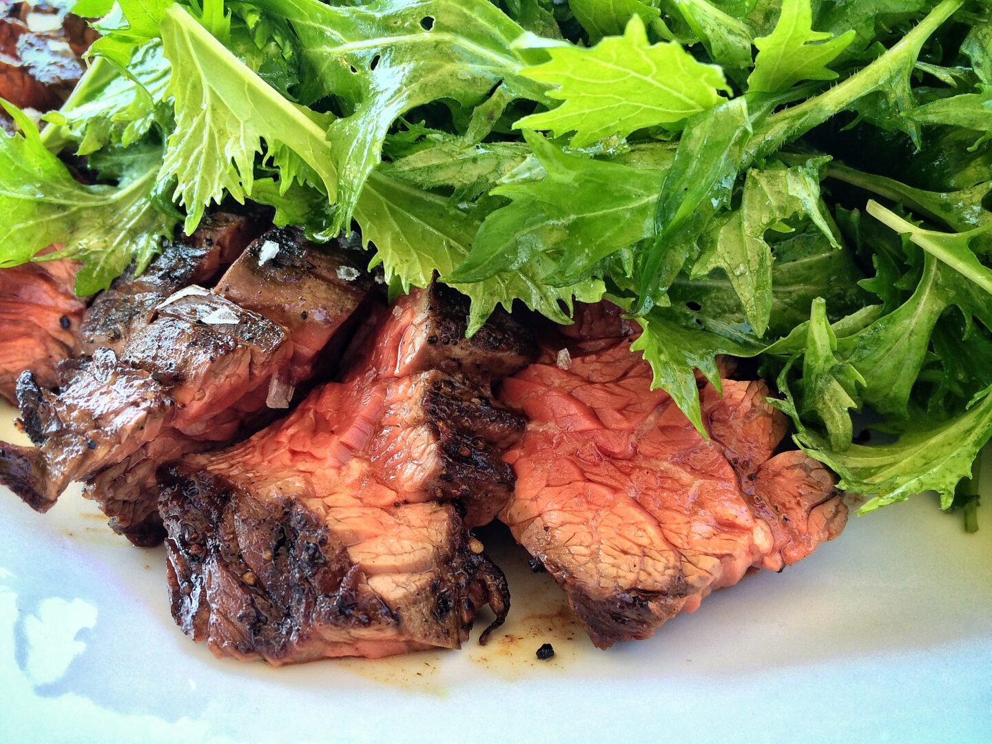 A steak on a plate with greens on it.