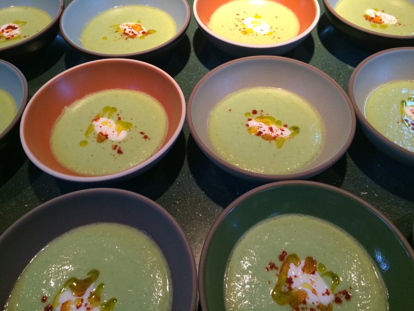 Several bowls of green soup are lined up on a table.