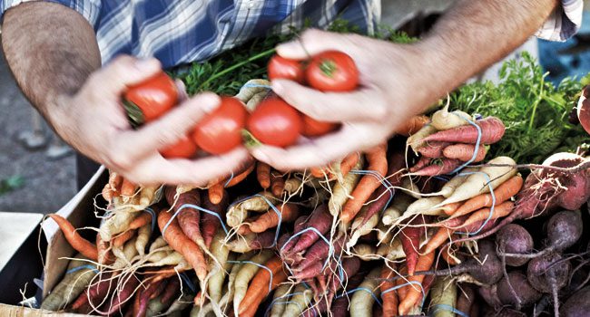 A man is holding a box of carrots and tomatoes.