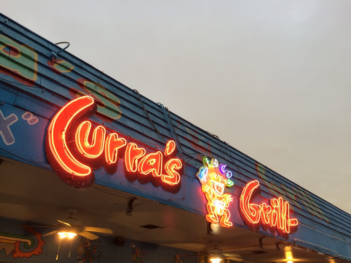 A neon sign for curra's grill on the side of a building.
