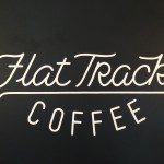 The logo for flat track coffee on a black wall.
