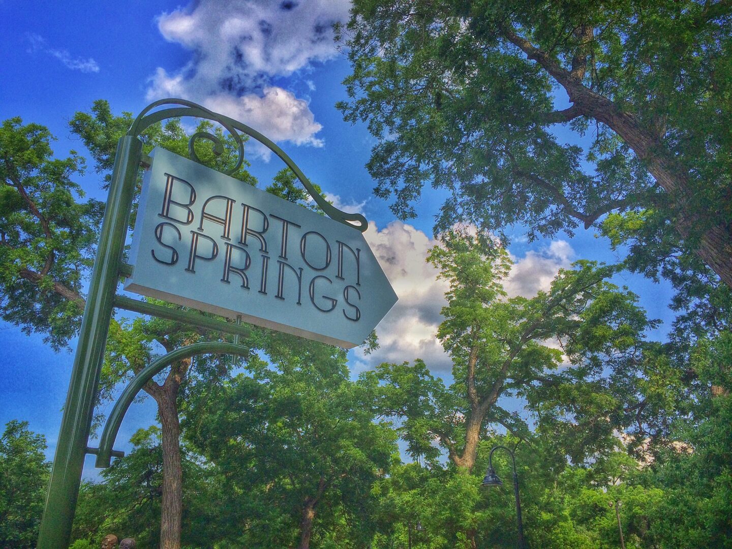 A sign for barton springs in front of trees.