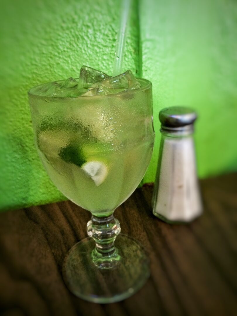 A glass of lime juice with a salt shaker next to it.