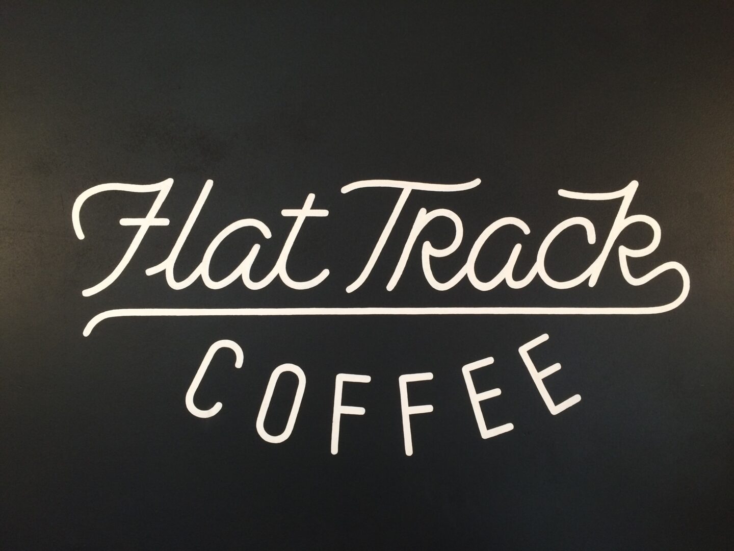 The logo for flat track coffee on a black wall.