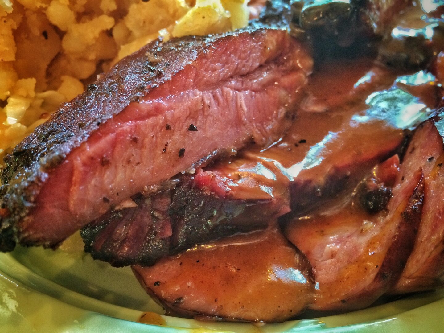 A plate of meat with gravy and corn on the cob.