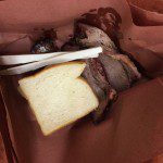 A piece of meat and bread in a brown paper bag.