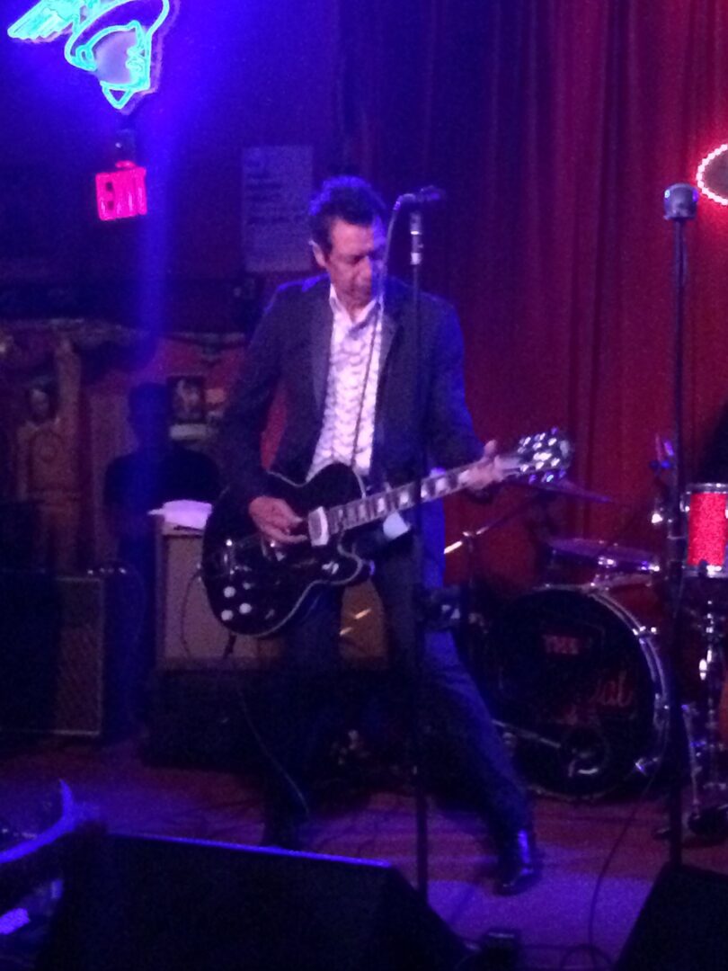 A man in a suit playing a guitar in a bar.