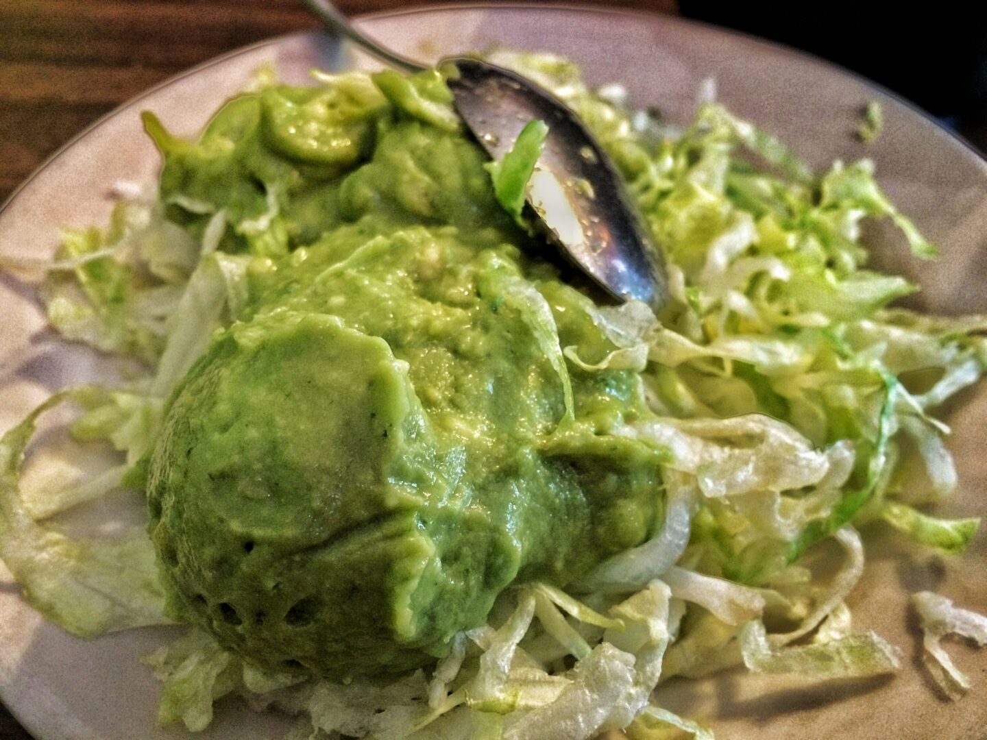 A plate of guacamole on a wooden table.