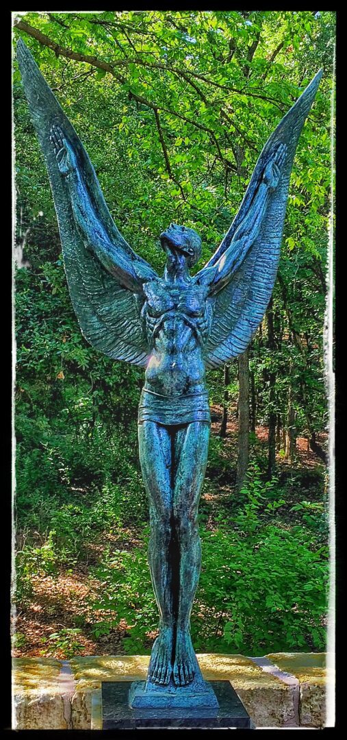 A statue of a woman with wings in the woods.