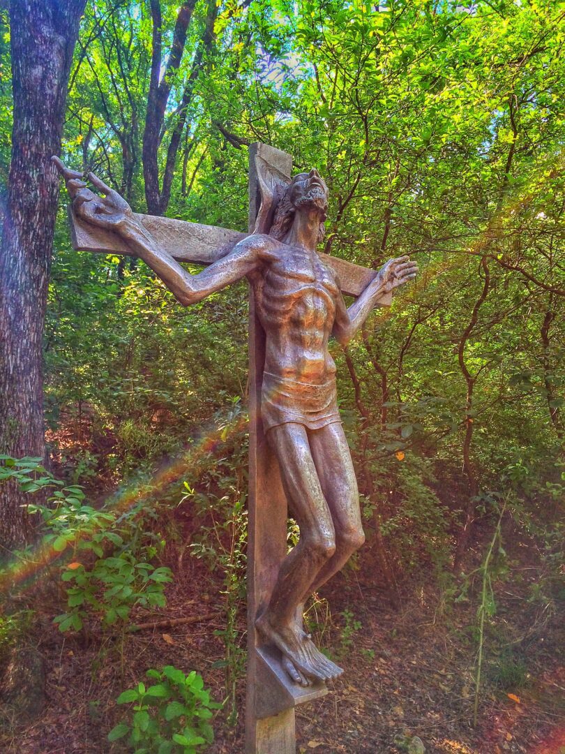 A statue of jesus on a cross in the woods.