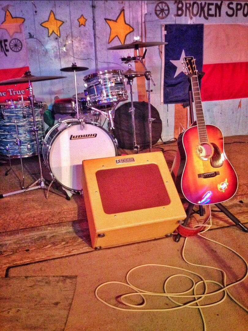 An acoustic guitar and a drum set in front of a texas flag.
