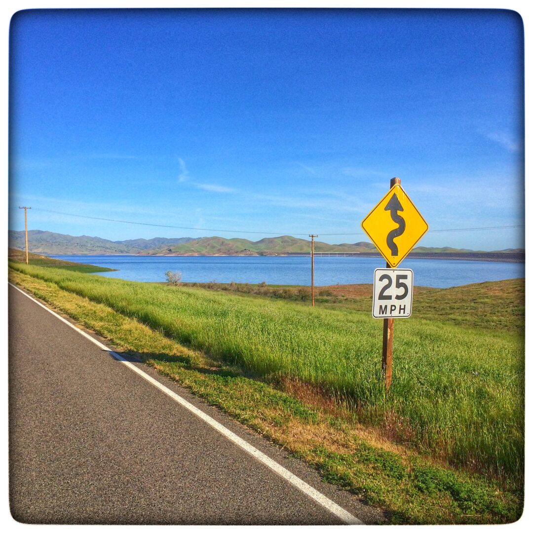 A yellow sign on the side of a road next to a lake.