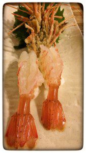 Two shrimp on a white plate with green leaves.
