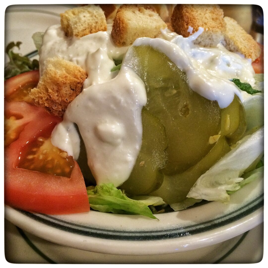 A salad with croutons, tomatoes and pickles.