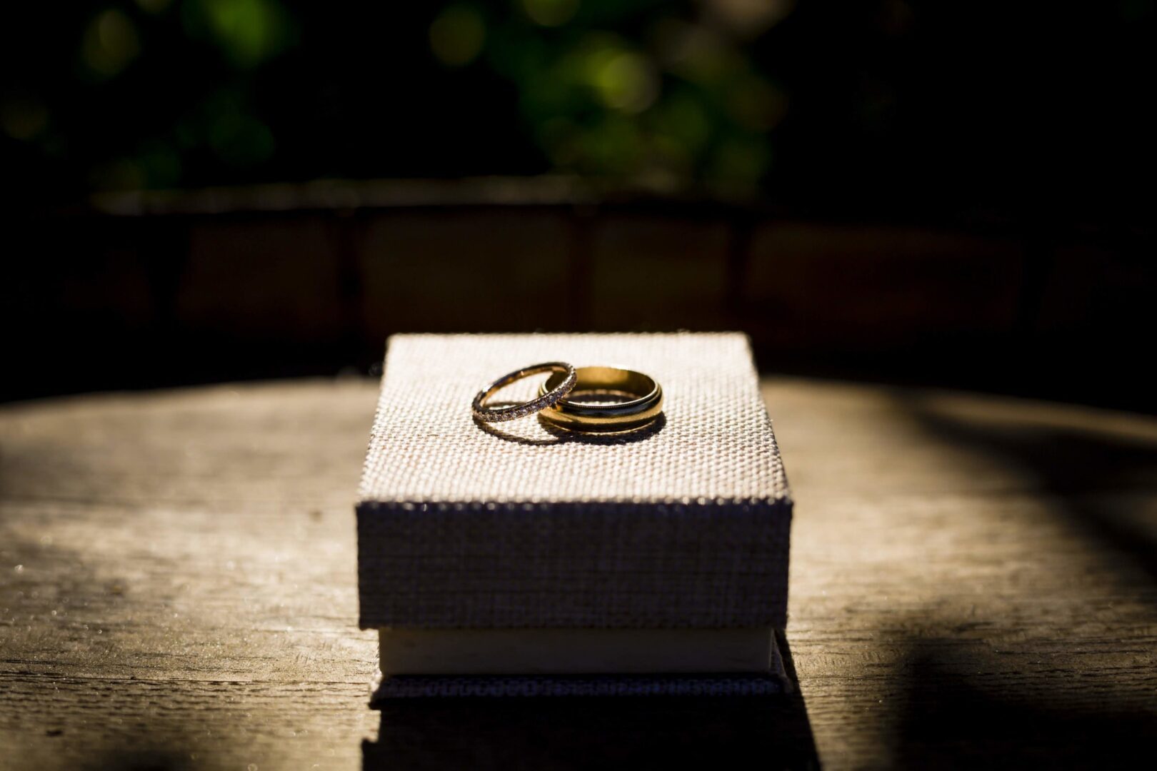 Two wedding rings in a box on top of a wooden table.
