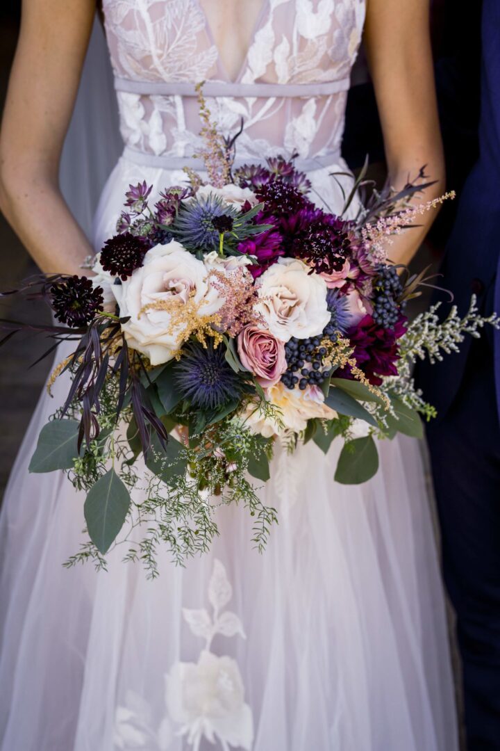 A bride holds a bouquet of purple and burgundy flowers.